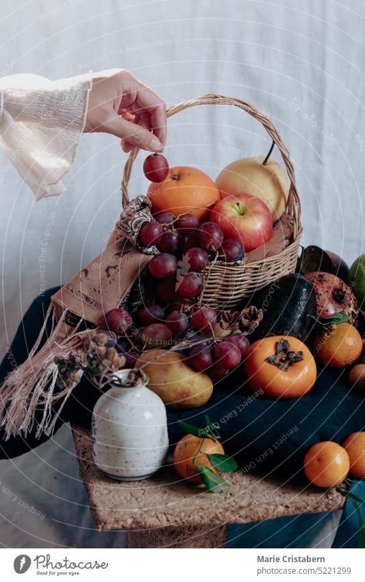 Vertical shot of dainty hand holding a grape over a table filled with twelve different round fruits, a Filipino belief and ritual to bring luck in the new year