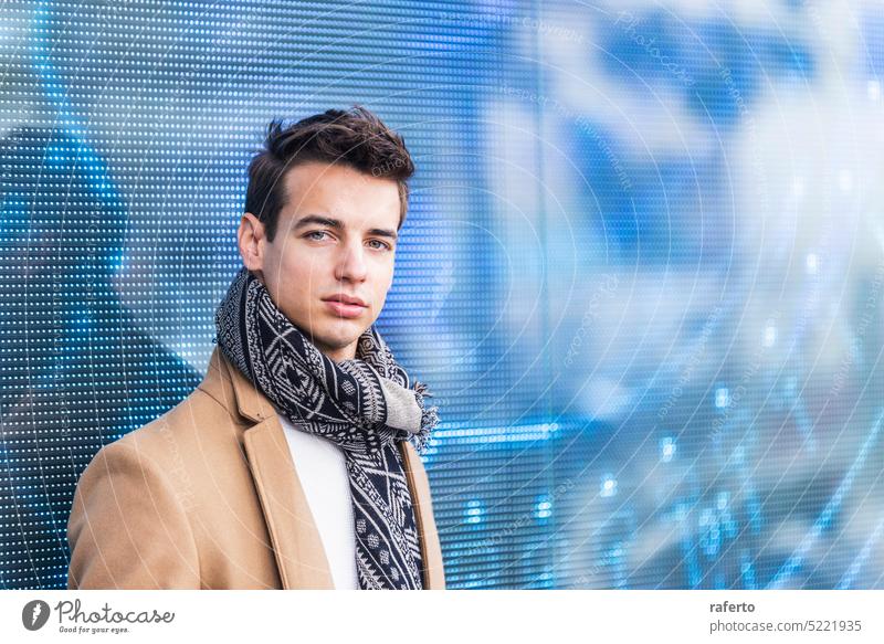 Portrait of stylish handsome young man with coat standing outdoors and leaning on led panel Adult Camera Caucasian Confidence Elegance Inspiration Jacket