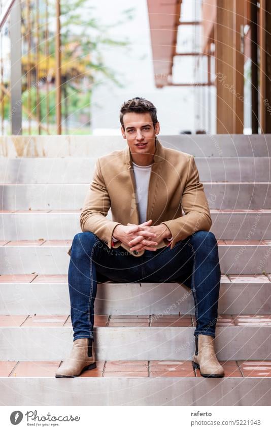 Portrait of stylish handsome young man with coat sitting outdoors Adult Camera Caucasian Confidence Elegance Inspiration Jacket Leaning Lifestyle Male Modern
