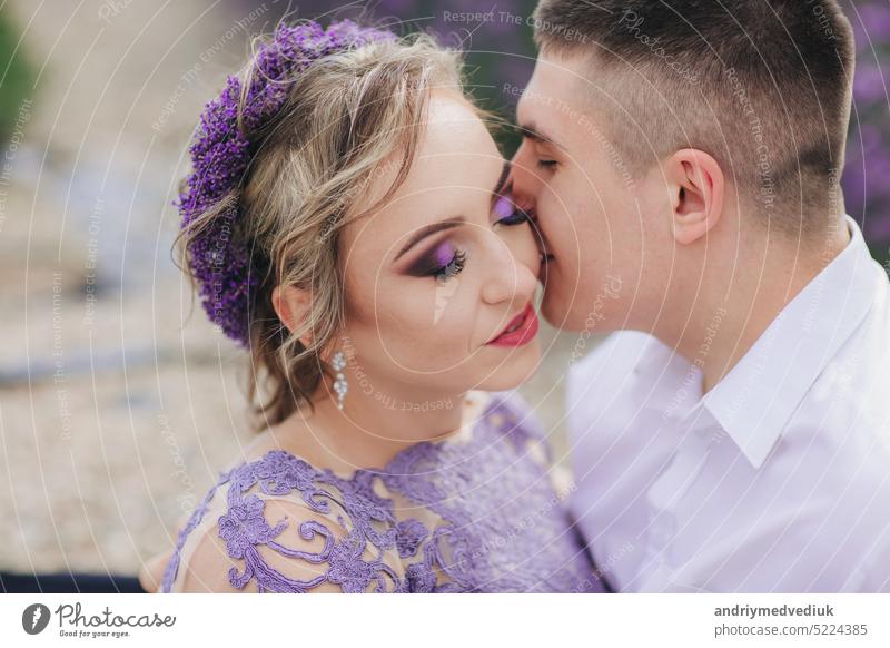 Young couple in love kissing in a lavender field on summer clody day. girl in a luxurious purple dress and with hairstyle people together beautiful young female