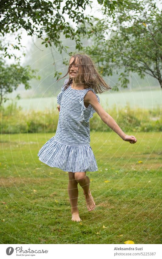 Happy cute little girl in sundress dancing and running on green lawn under the rain. Barefoot child enjoying  summer outdoors. beautiful carefree cheerful