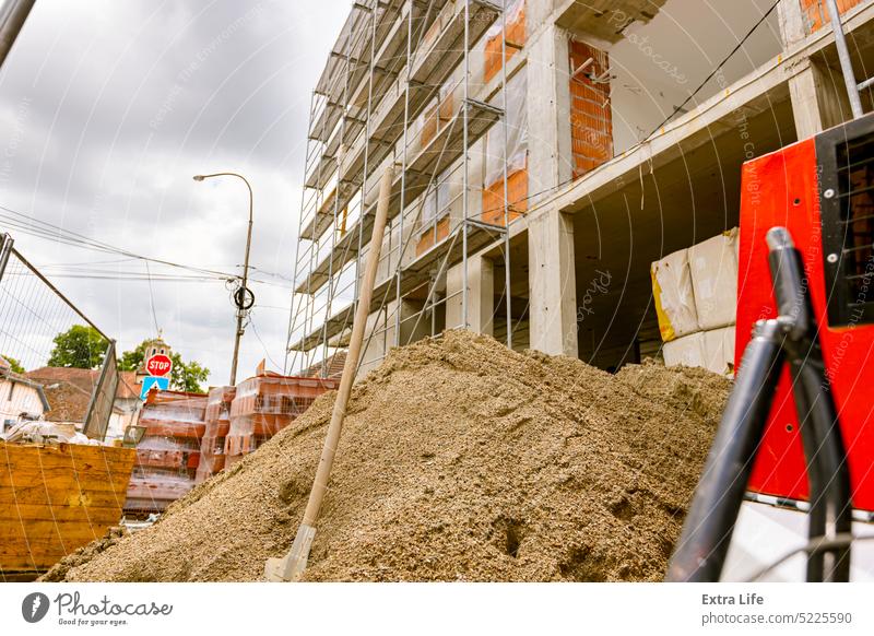 Shovel in the heap of gravel placed in front of residential building under construction with scaffold. Area Block Brick Build Building Site Civil Engineering