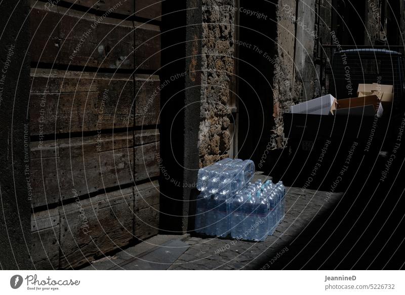 Water in pet bottles in front of old wall PET bottle Mineral water Refreshment Alley Old town Bottle of water Thirst Beverage Deliver delivery deposit Healthy