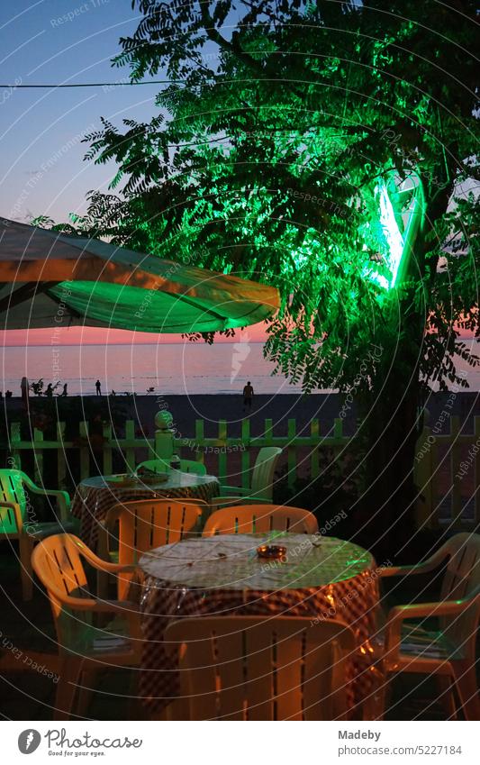 Terrace of a cafe with plastic chairs and oilcloth tablecloth with green lighting after sunset on the beach of Inkumu on the Black Sea near Bartin on the Black Sea coast in Turkey