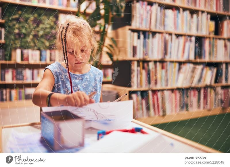 Schoolgirl doing homework. Elementary student learning, drawing pictures in school library. Primary student in school club. Back to school back schoolgirl