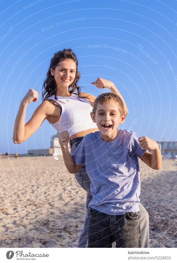 Happy Mother and son Showing strong arms on beach in a sunny day at sundet. Family together play sea sunset outdoor Toddler kid boy family Mom fun smile sand