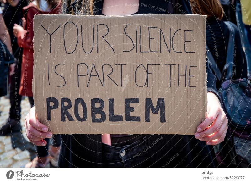 Your silence is part of the problem. English writing on a sign in the hand of a woman To be silent Keep quiet Looking away Negate keep out issue equality