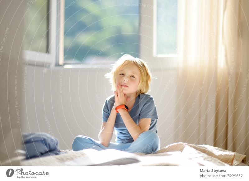 Portrait of cute schoolboy child in a blue tshirt in the bedroom on sunny day. Preteen boy sitting on the bed and dreaming. portrait preteen sunshine haircut