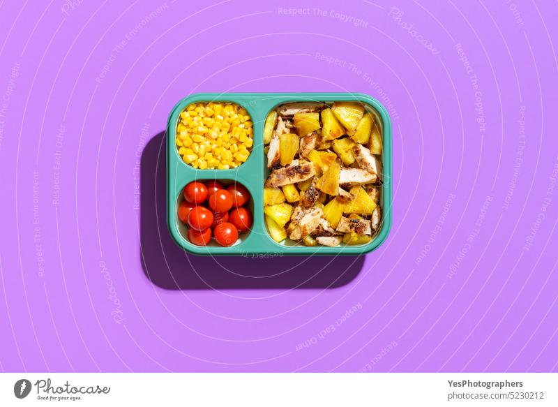 Summer salad in a lunch box, top view on purple background. Tropical dish in a silicone container. above bright cherry chicken color copy space corn cuisine