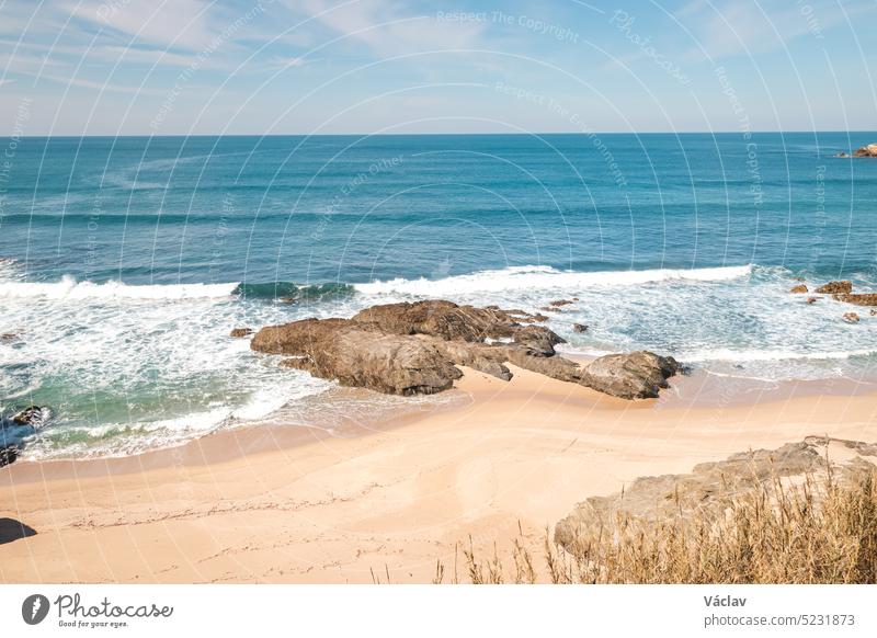 Rocks surround the sandy beach on the Atlantic coast near Vila Nova de Milfontes, Odemira, Portugal. In the footsteps of Rota Vicentina. Fisherman trail