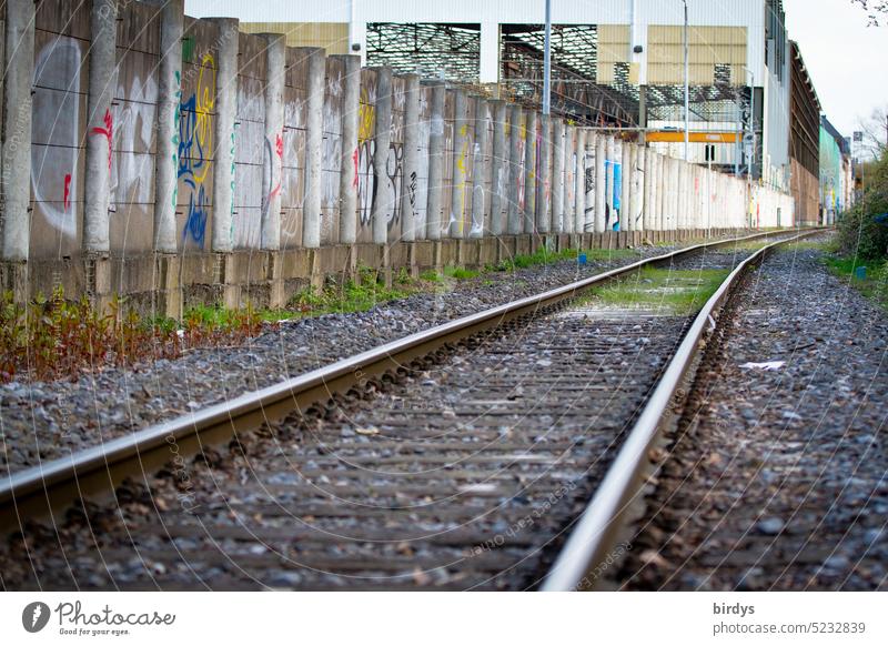 Railroad tracks along concrete wall in industrial area rails railway tracks Rail transport Concrete wall Industrial area Graffiti Industrial hall
