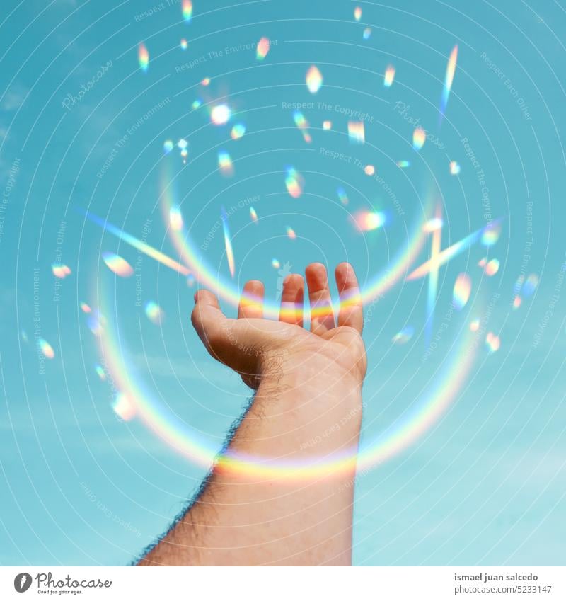 hand raised in the blue sky gesturing with the sunlight arm fingers hand up arm up arm raised skin palm body part rainbow flash sparkle flare lens flare