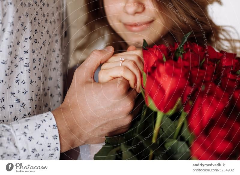 young man holding his fiance's hand with gold ring while making a marriage proposal with bouquet of red roses. Engagement of a young couple in love. The concept of love and togetherness.