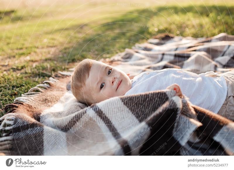 Happy adorable baby boy is lying on blanket on the grass in the park on summer day. Child in trendy and cute clothes meadow dandelion happy child beautiful fun