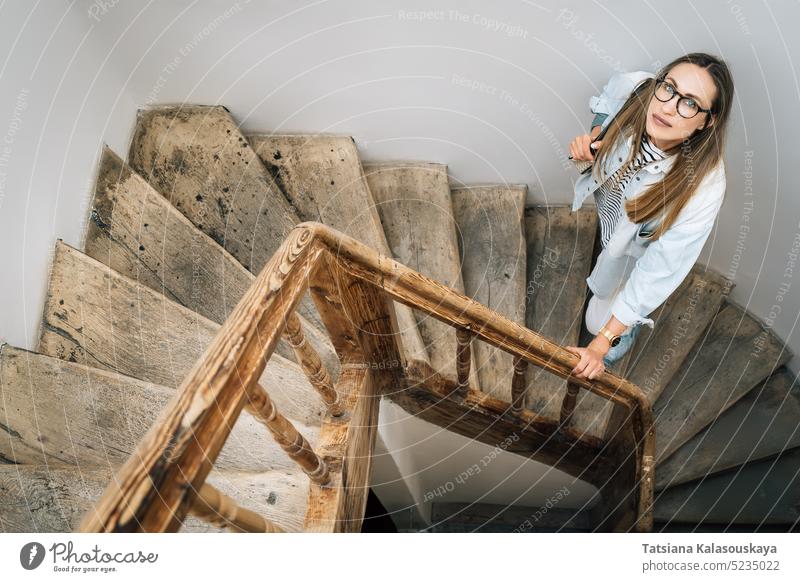 A woman looks up standing on an old wooden staircase look up looking up female people person adult one long-haired alone brown hair Attractive one person