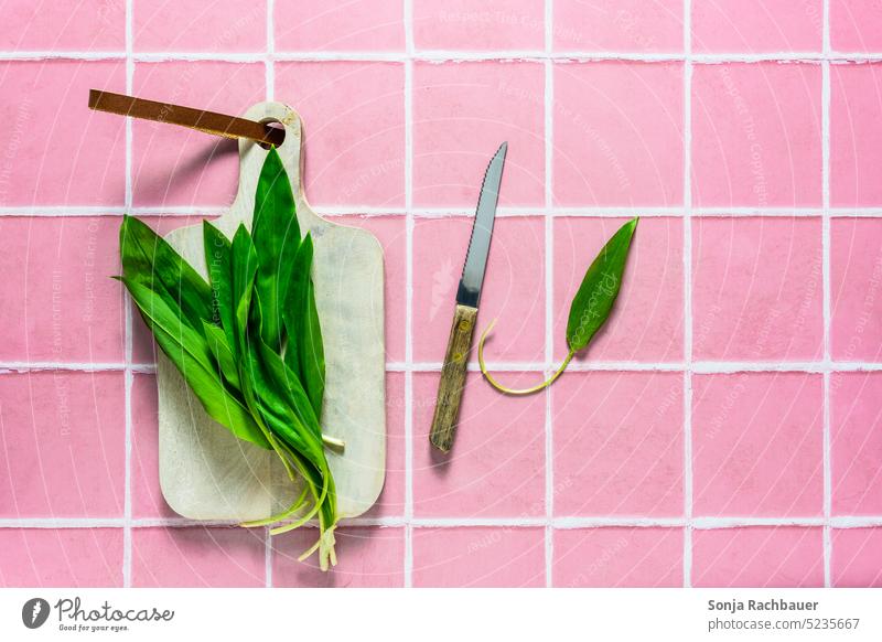 Fresh wild garlic on a cutting board. Pink tile background. Club moss Green Chopping board tiles plan Raw Vegetable Diet Ingredients Knives Cooking Wood