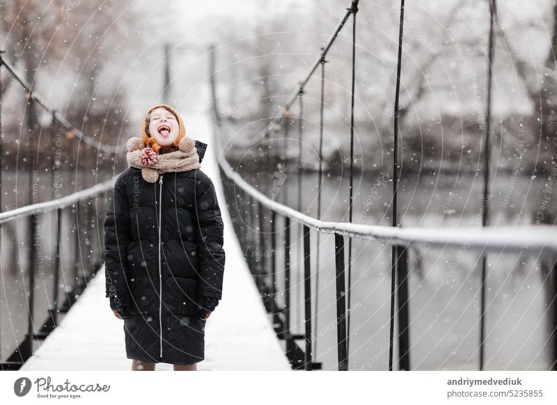 Funny little girl catches snowflakes in a beautiful winter park during a snowfall. Cute baby is playing in the snow. Winter activities for children. the winter holidays. happy childhood.