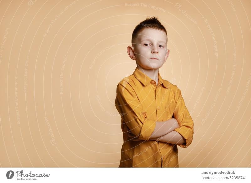 Photo of attractive cheerful nice school boy standing with his arms crossed in front of camera while isolated on yellow background. High quality photo child fun