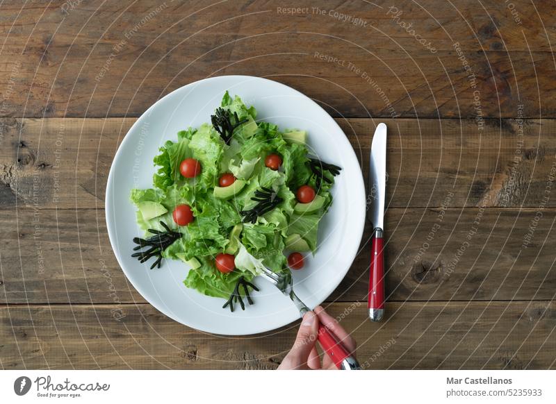 Hand with fork eating assorted salad on white plate on wooden background. Copy space. vegetable veggie vegetarian detox nature raw ingredient trend seaweed