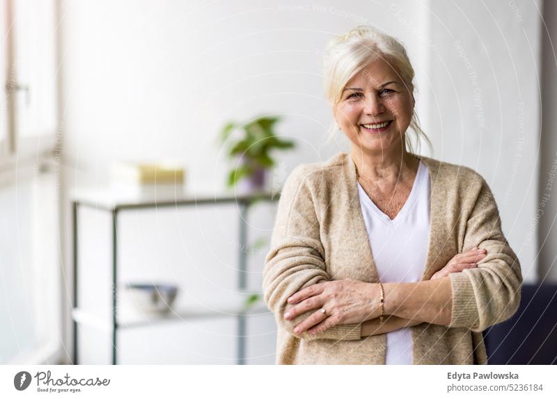 Portrait of smiling senior woman standing with arms crossed real people indoors loft window home mature adult one person attractive successful confident