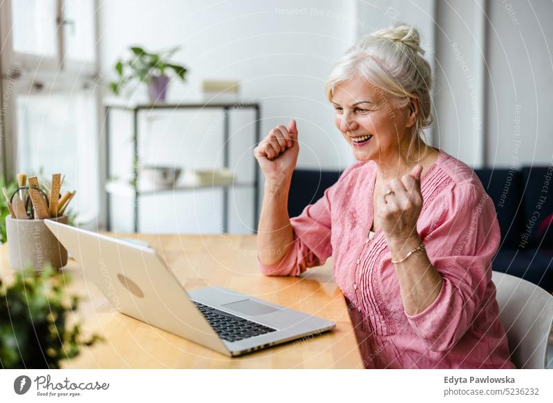 Cheerful senior woman using laptop in the living room at home real people indoors loft window mature adult one person attractive successful confident beautiful