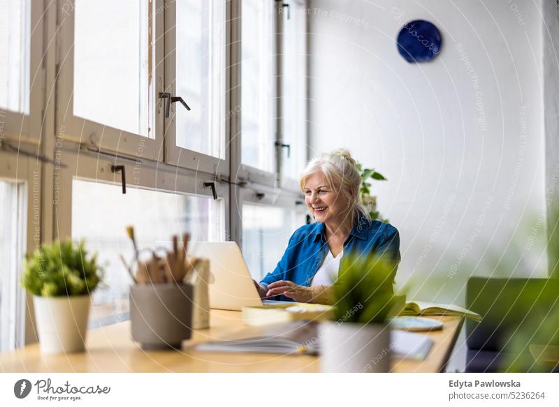 Portrait of smiling mature businesswoman using laptop at desk in office real people senior indoors loft window home mature adult one person attractive