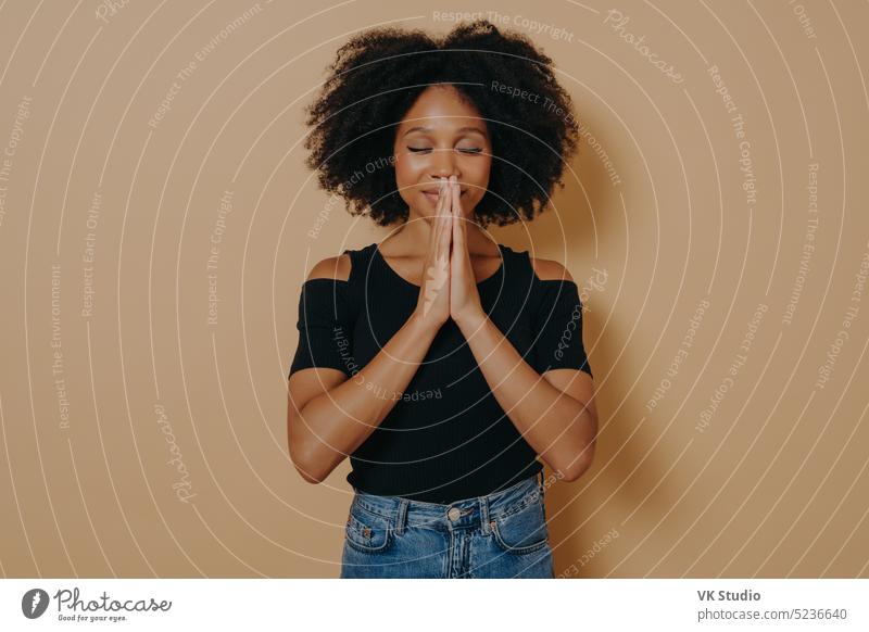 Afro American young woman praying and holding hands in prayer gesture standing in studio afro american african believe asking luck black lady hope god posing