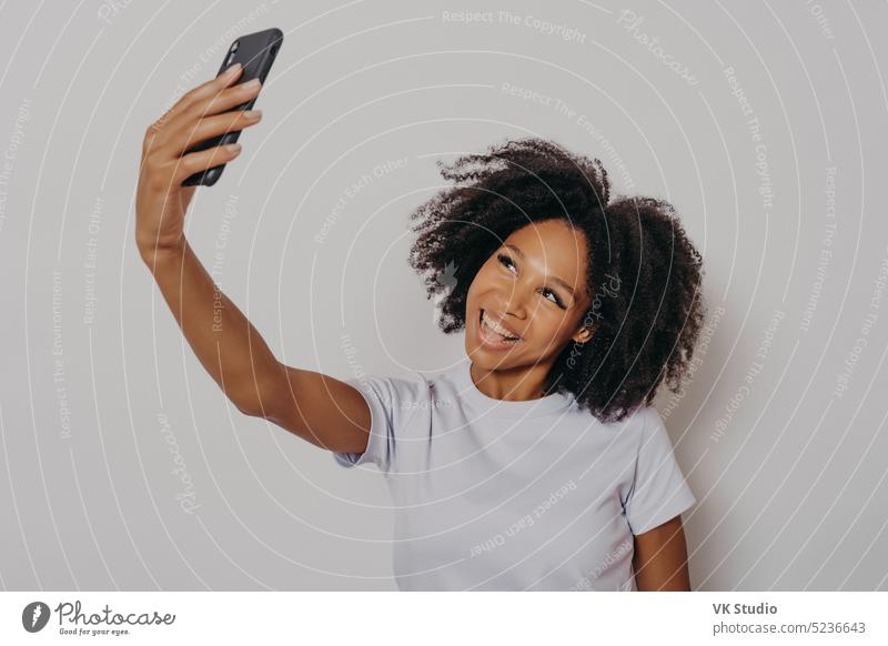 Cheerful young african woman with curly hair taking selfie on her modern mobile phone afro american photo background smartphone making people beautiful