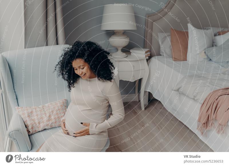 Lovely african american enjoying happy pregnancy while sitting in bedroom pregnant mixed race young woman baby love child abdomen maternity mom mother