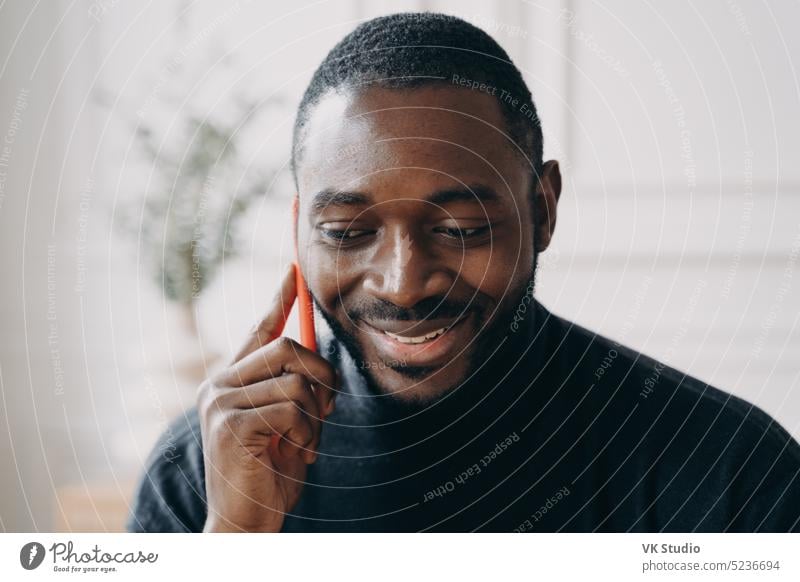 Cheerful young African American businessman talking on smartphone while working distantly at home african american holding smiling conversation mobile office