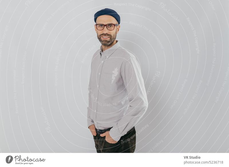 Profile shot of attractive unshaven man dressed formally, wears optical glasses, models over white background, happy to achieve good results at work, has pleased facial expression. People and style