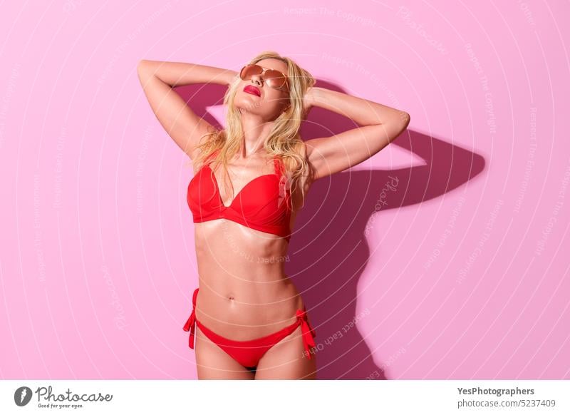 Woman in a red swimsuit against a pink background. Blonde woman in bright light. 50s beach beauty bikini blonde body bra color concept cool design elegant enjoy