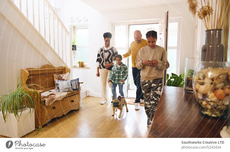 Family arriving home with pet dog, girl using phone family happy door people interior arrive excitement multiracial hallway togetherness lifestyle parent child