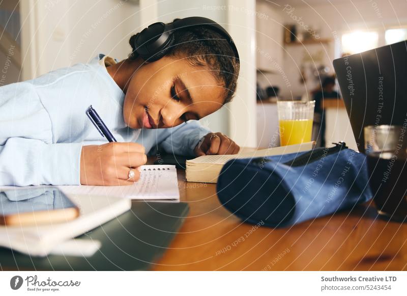 Teen girl doing homework wearing headphones teen study cell mobiles listen concentration write notebook pen learning education multiracial lifestyle indoor day