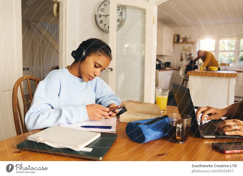 Teen girl doing homework wearing headphones, using phone teen study cell mobiles listen concentration notebook learning education four multiracial lifestyle