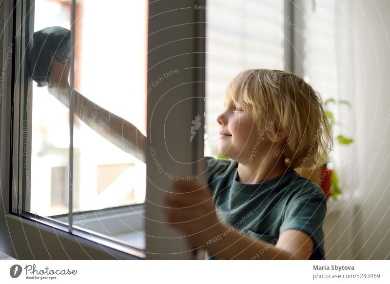 Cute little boy washing a window at home. Child helping parents with household chores, for example, cleaning windows in his house. Children doing housework.