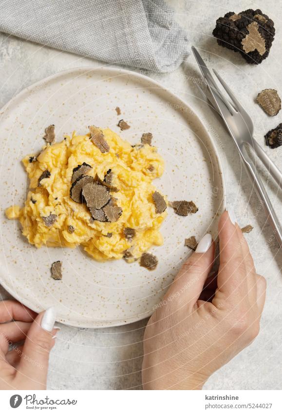 Hands with plate with Scrambled eggs with fresh black truffles top view, gourmet breakfast sliced Italy hands fork knife Italian cousine yellow white food