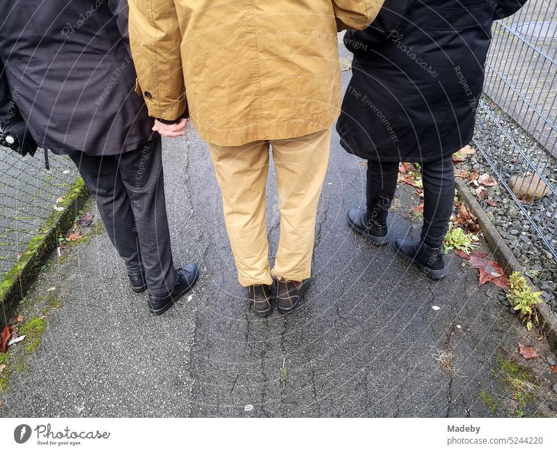 Women of different ages with jackets and coats in beige and black walking on wet asphalt in Oerlinghausen near Bielefeld at the Hermannsweg in the Teutoburg Forest in East Westphalia-Lippe