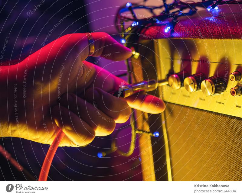 Man plugging jack into the guitar amplifier, closeup, for music, entertainment themes. Neon colorful light concert loud sound speaker studio background bass