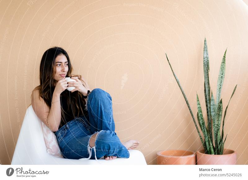 barefoot young woman in casual clothing relaxing with a cup of coffee on the orange colored terrace beberage casual clothes day enjoy girl jeans orange wall