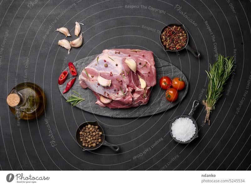 A piece of pork ham on a black board and spices olive oil, salt, rosemary branch and pepper garlic food slice butcher ingredient sirloin meal bottle raw part