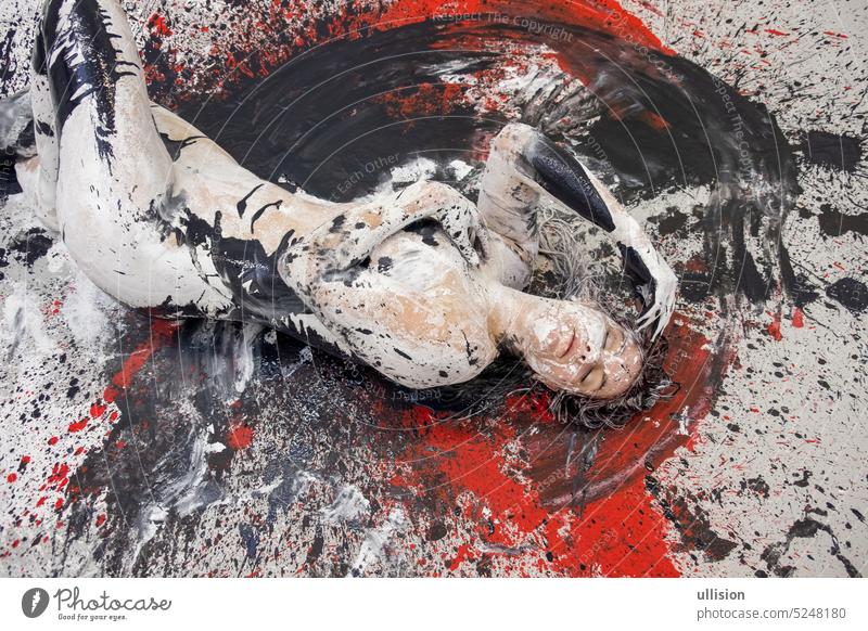 Young artistically abstract painted naked woman with black and white paint, lying on the red, black, gray designed floor in the studio copy space young nude