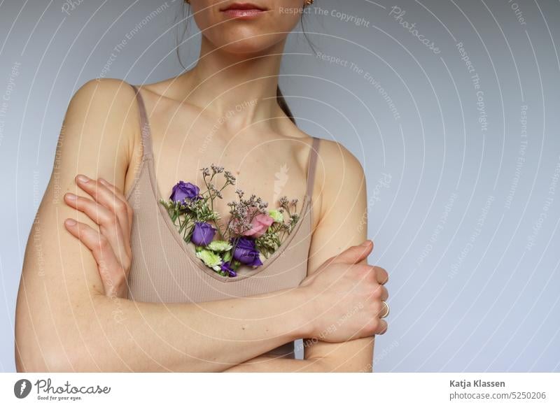 A young woman with crossed arms and in a beige chest holder in which colorful flowers. Young woman Woman Chest holder Arm Flowers in chest holder
