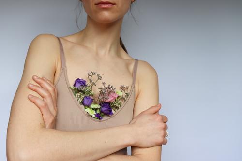 A young woman with crossed arms and in a beige chest holder in which colorful flowers. Young woman Woman Chest holder Arm Flowers in chest holder