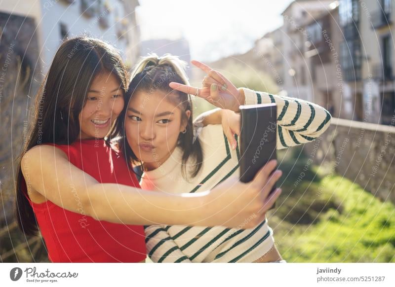 Smiling Asian girlfriends taking selfie on street women smartphone together shoot cheerful take photo happy gesture rock using ethnic device female share smile