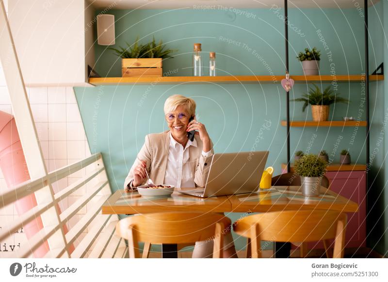 Senior woman using mobile phone while working on laptop and having healthy breakfast in the cafe aged call coffee coffee shop coffeehouse communication