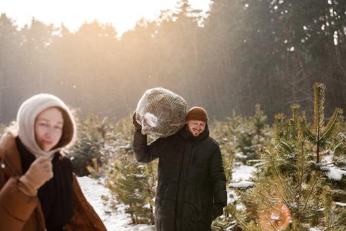 Love romantic young couple woman, man in snowy winter forest with fir tree. Walking, having fun, laughing in stylish warm clothes. Snow lovestory. Romantic date, weekend. Happy Christmas and New Year