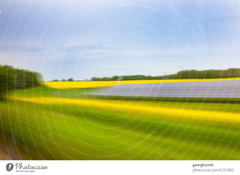 solar canola drive | Photo from a train or car drive past a meadow and canola field, as well as solar modules. In the background wind turbines are visible, in the foreground color spectra of the laminated glass.