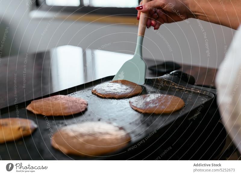 Anonymous adult housewife cooking pancakes on griddle woman breakfast flip appliance pour batter fry spatula counter kitchen domestic make home appetizing