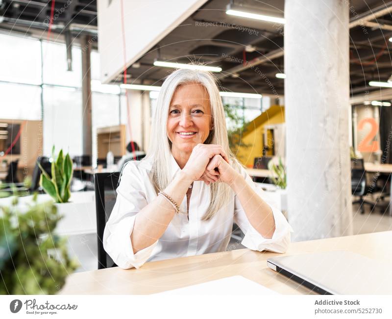 Cheerful senior female employee sitting at table in office woman laptop at work modern business workspace job company businesswoman positive smile aged elderly